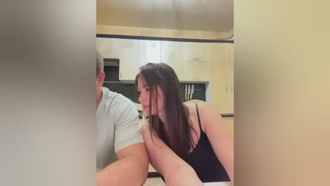 Media: A candid video captures a woman in a black tank top kissing a man in a light gray shirt in a modern kitchen.