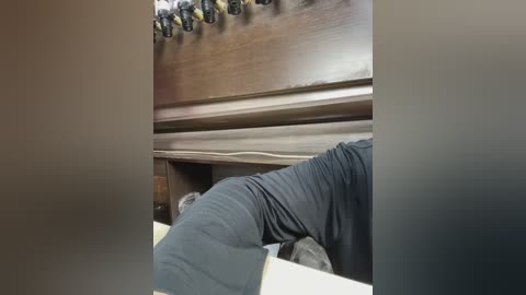 Media: Video of a person wearing black pants, bending over to reach into a drawer in a wooden cabinet. The background shows a dark wood finish with a collection of small black and yellow objects.
