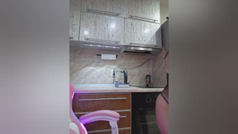 Media: Video of a compact, modern kitchen with white cabinets, beige marble backsplash, stainless steel appliances, and a white chair partially visible on the left.