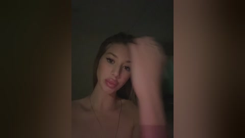 A video of a young Asian woman with straight, shoulder-length black hair, wearing a strapless top, looking introspective, with her hand covering her face.
