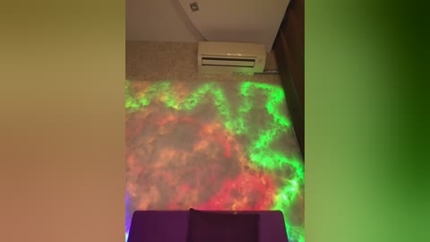 Video of a dimly lit room with a beige carpet, featuring a large, colorful nebula-like pattern projected on the floor from a laser light show. An air conditioner is mounted on the wall above.