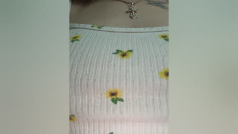 Video of a person wearing a white ribbed tank top with yellow sunflower print, showcasing a tattoo on the neck and a silver cross necklace.