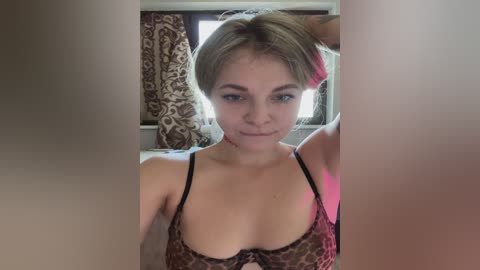 A video of a light-skinned woman with short blonde hair, wearing a leopard-print bra, sitting indoors. She has a small nosebleed on her right cheek.