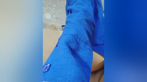 A video of a person's thigh in a bright blue dress, with a small blue button on the side, set against a light-colored background with a patterned wall in the background.