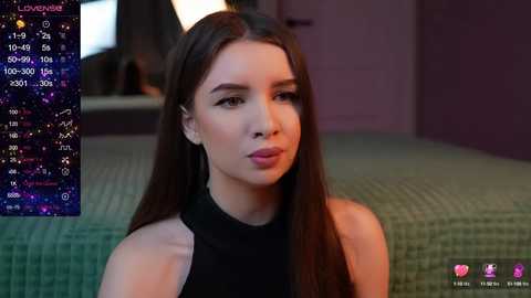 Media: Video of a young woman with long brown hair and fair skin, wearing a black sleeveless top. Background shows a green bedspread and a purple wall. A digital clock displaying \"Loverine\" is visible on the left.