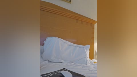 Video of a neatly made bed with white pillows and a wooden headboard, partially covered by a black book titled \"The Hobbit.\" Warm, golden light casts a cozy ambiance in the room.