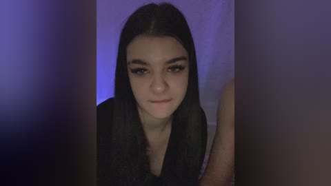 Video of a young woman with long black hair, fair skin, and dark eyebrows, wearing a black top, taken indoors with a blurred background and soft lighting.