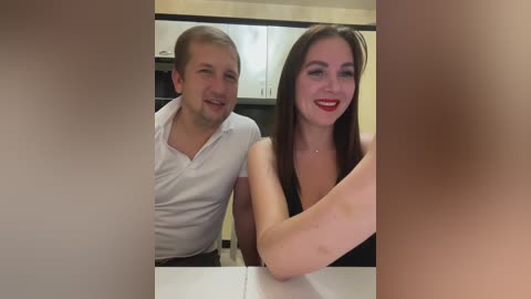 Media: Video of a smiling couple in a modern kitchen; man in white shirt, woman in black top. Background features white cabinets and beige walls.