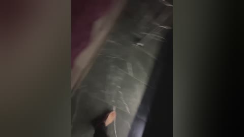 A video shows a person wearing a black hoodie and jeans, standing in a dimly lit room with blurred, darkened walls. The image is slightly out of focus, capturing a candid, indoor moment.