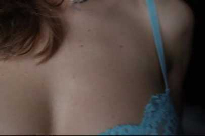 Media: Video of a woman's bare back with light skin and faint acne marks, wearing a blue lace bra. Her light brown hair is partially visible. Background is dark and indistinct.