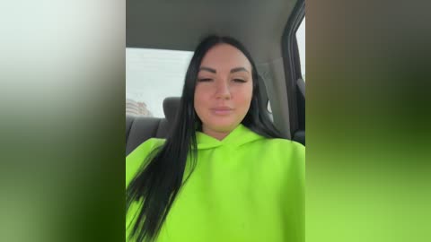 Video of a woman with long black hair, wearing a bright neon green surgical cap, sitting in a car with a blurred background.