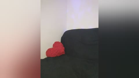 Media: Video of a red plush heart on a black couch against a white wall, with a blurred, gradient background transitioning from red to black.