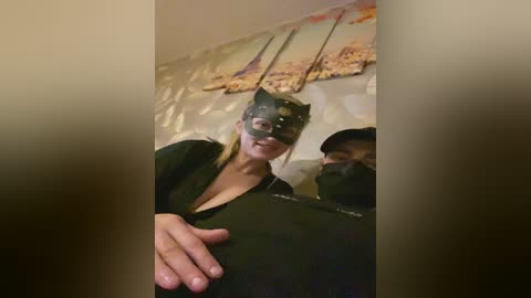 Video of a woman wearing a black Batman mask and black clothing, holding a phone. The background features abstract art and a blurred figure.