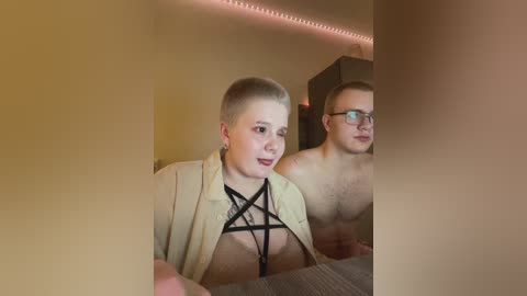 Video of two shirtless, young, fair-skinned men in a dimly lit room, one with a short, light brown mohawk, wearing glasses, and the other with short blond hair, standing side by side.