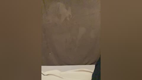 A video of a person's bare, pale buttocks, partially obscured by a beige towel draped over the lower half. The skin appears smooth and slightly shiny, with a hint of hair. The background is plain and neutral.