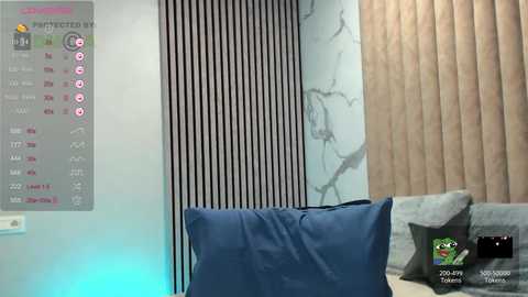 A video of a modern, minimalist bedroom with a blue cushion on a light grey bed, a wooden panel wall, and a digital clock showing 8:45 AM.