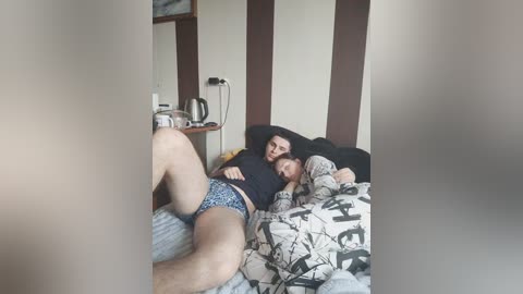 Video of a couple sleeping in a dimly lit room, with the man's leg visible, wearing blue shorts, and the woman in a patterned nightgown. Background includes wooden panels and a framed picture.