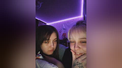 Media: Video of two young women, one with long dark hair, the other with short blonde hair, smiling closely together in a dimly lit room with purple LED strip lights.