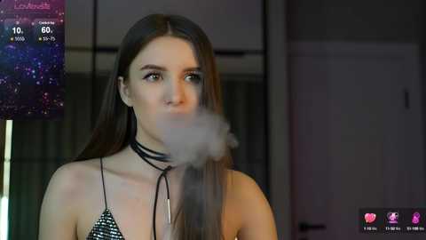 Media: A video of a young woman with long brown hair, wearing a black choker and a black and white polka-dot bikini, blowing a large cloud of smoke into the air.