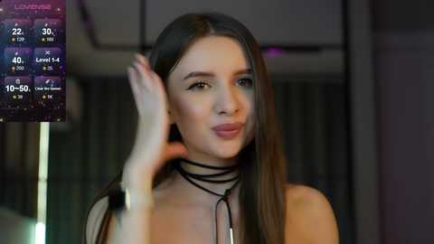 Media: Video of a young woman with straight brown hair, wearing a black choker necklace, looking at her phone, in a dimly lit room with a digital clock display.