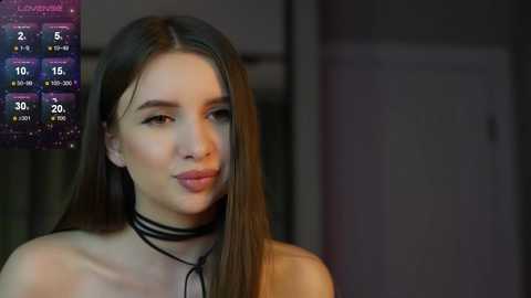 Media: Video of a young woman with straight brown hair, wearing a black choker, in a dimly lit room. Weather forecast overlay in the top left.