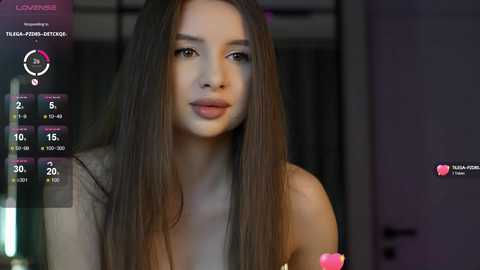 Media: Video of a young woman with long, straight brown hair, fair skin, and a slim figure, wearing a light gray sleeveless top. Background features a dimly lit room with indistinct objects.