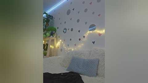 Video of a cozy, dimly lit bedroom with white walls adorned with heart decals, a plush white sofa, a soft grey cushion, and fairy lights.