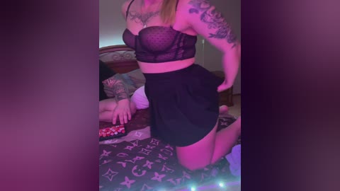 Media: A video of a woman in black lingerie and high-waisted shorts, kneeling on a bed with a Louis Vuitton-patterned duvet. Her left arm is adorned with tattoos. The room is dimly lit with a pinkish hue.