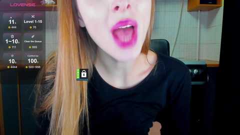Video of a young woman with long, straight, blonde hair, wearing bold pink lipstick, open-mouthed, in a black top, in a tiled kitchen.