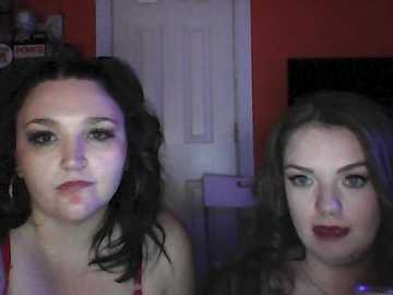 Video of two women with dark hair, one with red lipstick, the other with blue lipstick, in a dimly lit room with purple lighting.