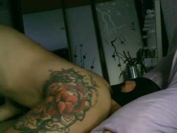 A video shows a person with a large, colorful tattoo of a rose on their back, lying on a bed with a purple pillow, surrounded by Asian-inspired artwork.