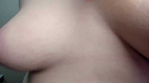 Video of a light-skinned woman's bare chest, focusing on her large, natural breasts with visible nipples, set against a neutral background.