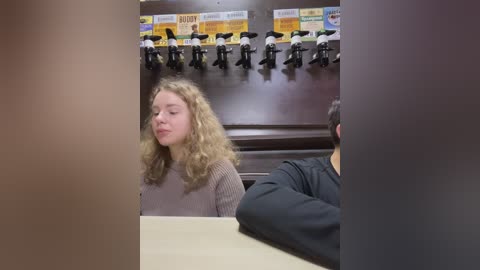 Media: Video of a young girl with curly blonde hair, eyes closed, smiling, standing in front of a row of black microphones labeled with colorful signs on a dark wooden wall.
