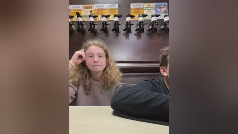 Media: A video of a girl with curly blonde hair and a serious expression, seated in a classroom with other students, all facing a teacher's desk.