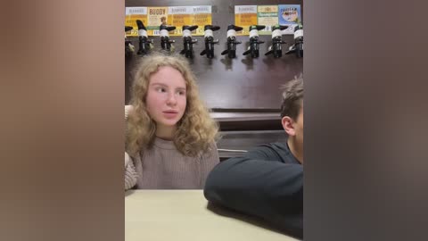 Media: Video of a classroom with a blonde girl with curly hair in a beige sweater and a boy in a black shirt facing a projector screen displaying a \"Burger King\" advertisement.