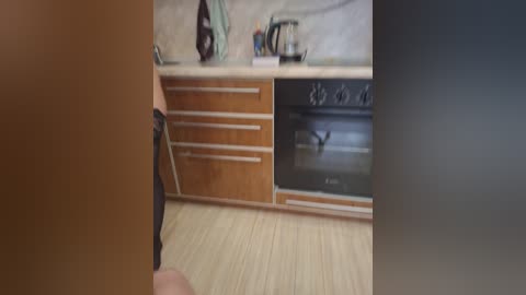 Media: A video of a modern kitchen with light wooden cabinets, a stainless steel stove, a black kettle, and a wooden floor. The image is slightly blurred.