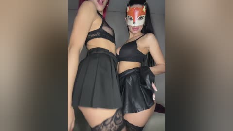 Video of two women in matching black lace lingerie, one with red hair, the other with long black hair, posing provocatively indoors.