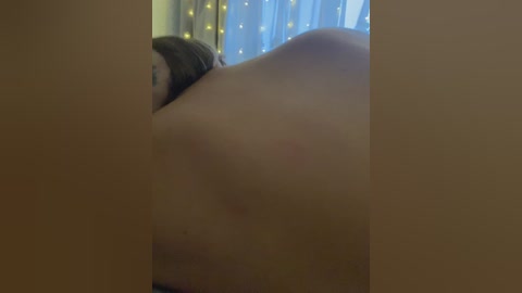 Media: A video of a woman lying face down on a bed, her naked back visible, with a tattoo on her right shoulder. The background features a curtain with fairy lights.