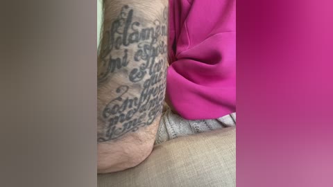 Media: Video of a person's arm tattooed with a detailed script and wearing a bright pink shirt, sitting on a beige couch.