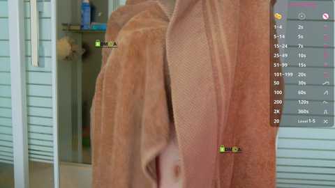 Video of a person with medium-brown skin wrapped in a brown towel, standing in front of a gray house with a sliding glass door. The towel has green dots for tracking.