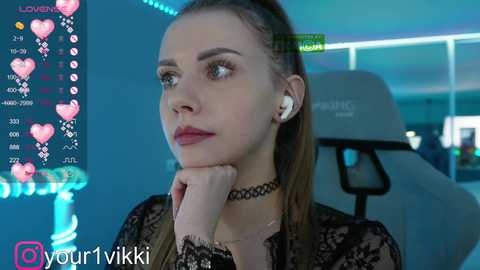 Media: Video of a young woman with fair skin and long brown hair, wearing a black lace top and choker, looking thoughtful in a modern room with a green exercise bike and blue LED lights.