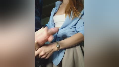 Video: A light-skinned woman with red hair, wearing a blue shirt and beige skirt, holds a hard penis.