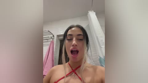 Media: Video of a young woman with long, straight black hair, wearing a red halter bikini, standing in a white-tiled bathroom with a shower curtain and towels. She has a light complexion and is mid-scream.