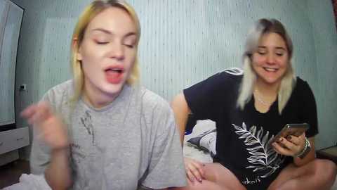 Media: Video of two women, one blonde, one brunette, laughing, in a bedroom with a light green wall and a white dresser.