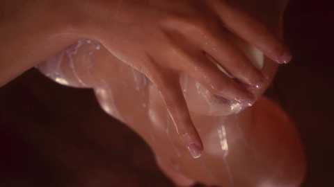 Media: A close-up video of a hand holding an orange, translucent dildo with clear, viscous fluid dripping from it, against a dark, blurred background.