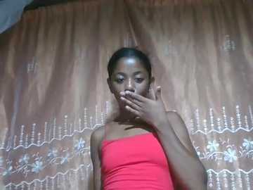 A video of a young Black woman with a dark complexion, wearing a bright pink tank top, covering her mouth with her right hand, standing in front of a beige, floral-patterned curtain.