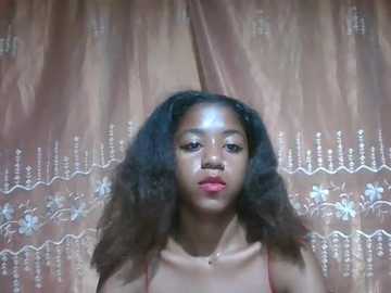 Video of a young African American woman with curly hair, wearing a red top, standing in front of a pink, sequined curtain with intricate patterns.