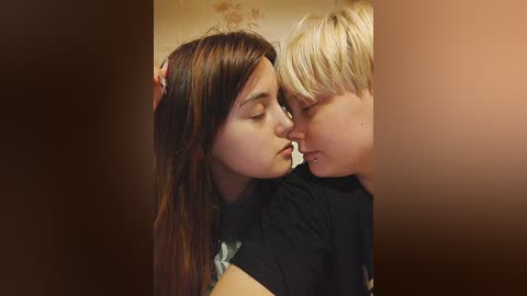 Media: A video shows two young girls, one with long brown hair, the other with short blonde hair, kissing tenderly in a dimly lit room with wallpaper.