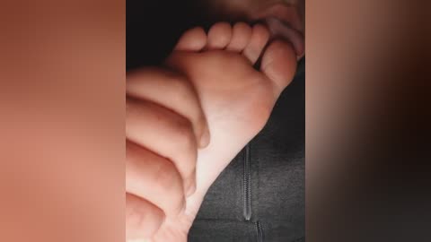 A close-up video of a person's bare foot, with a wrinkled sole and toes slightly curled, resting on a dark gray fabric surface, possibly a couch. The skin is light-toned, and the background is blurred.