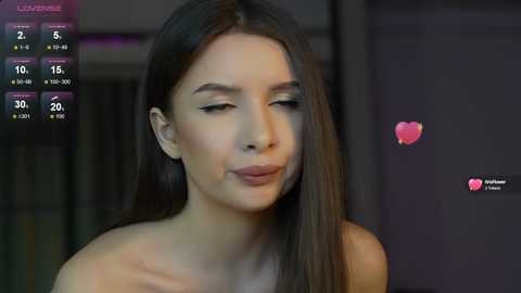 Media: A video of a woman with long, straight brown hair, fair skin, and closed eyes, wearing a strapless top, with a heart emoji overlay, in a dimly lit room.